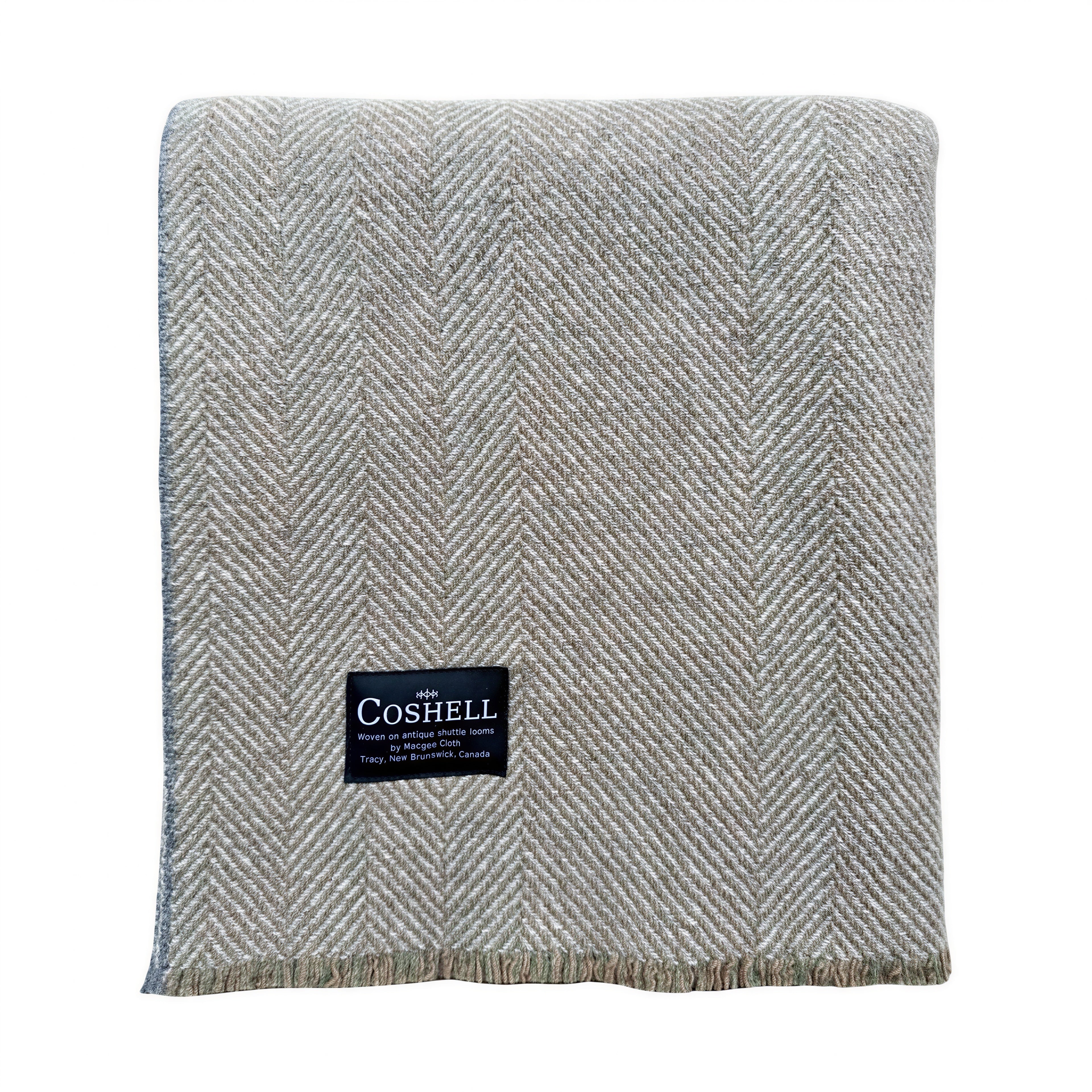 A folded herringbone-patterned woven throw blanket in a light gray with orange and green weft, featuring a black Coshell brand label on the front.