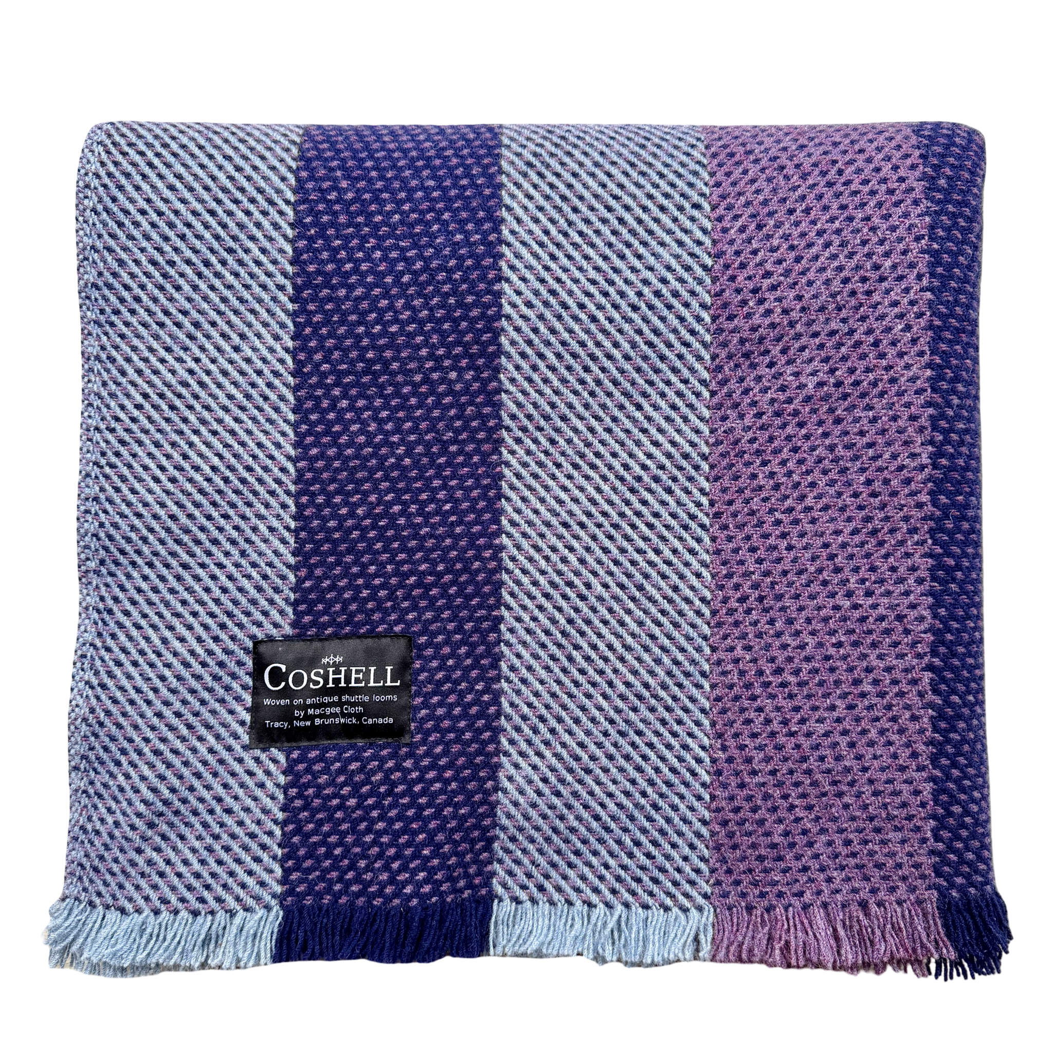A square woven throw blanket with vertical stripes in light blue, dark purple, and lavender purple, finished with fringe on one side. A black Coshell brand label is sewn onto the front.