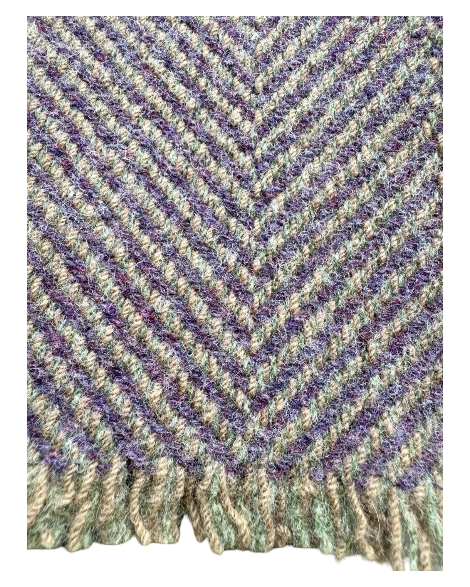 A close-up of woven wool textile with a herringbone pattern in mixed purple, brown, and sage green tones, finished with a fringed edge.