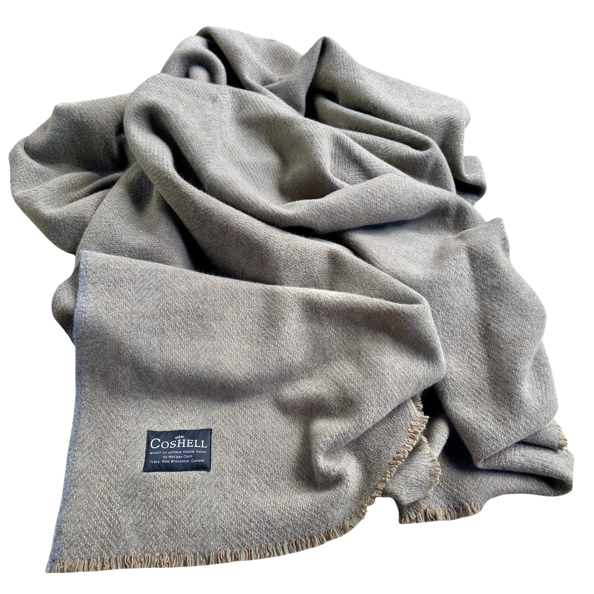A light gray orange and green warp woven blanket with fringed edges and a dark blue Coshell label, draped in soft folds