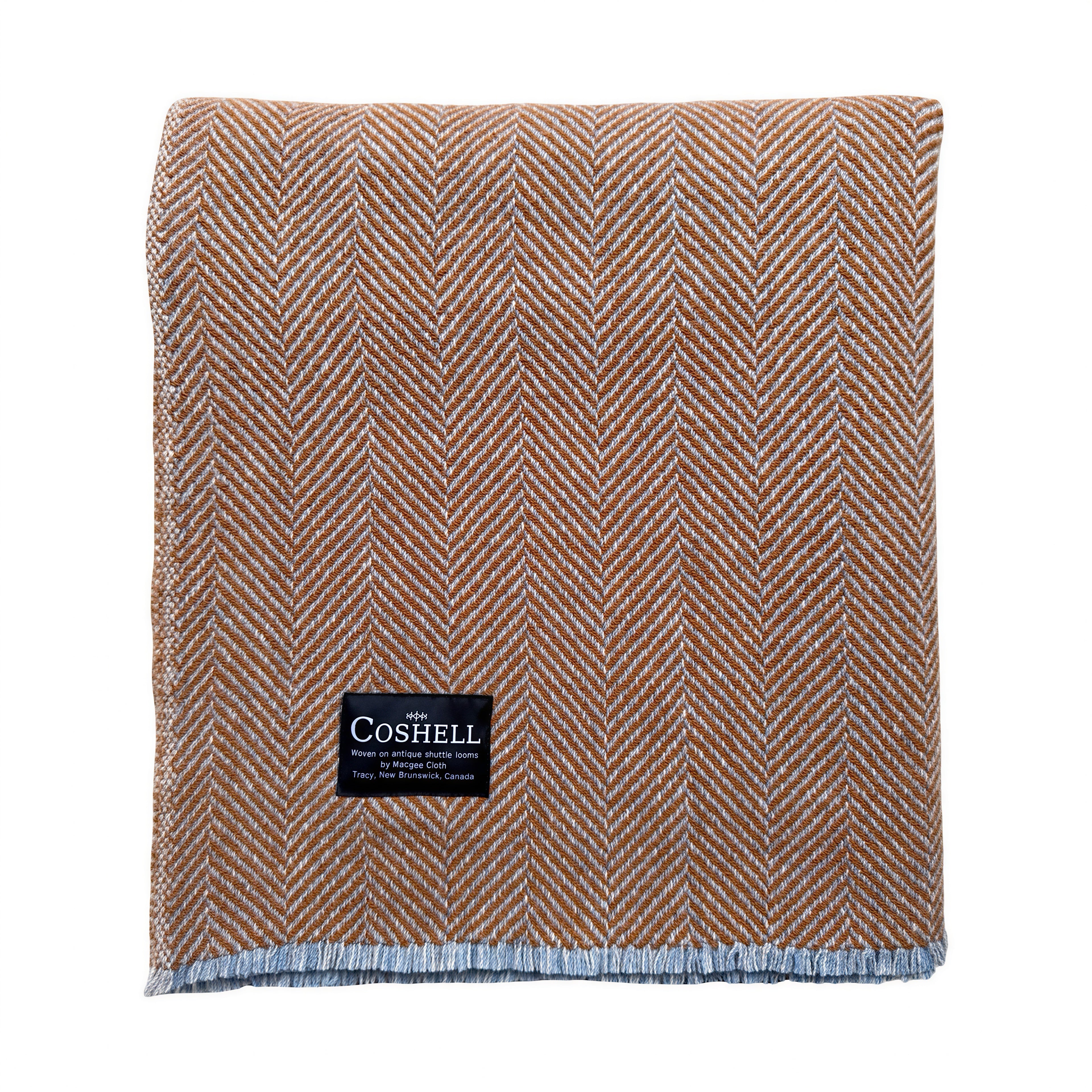 A folded orannge with grey and blue weft herringbone woven throw blanket with a black Coshell brand label