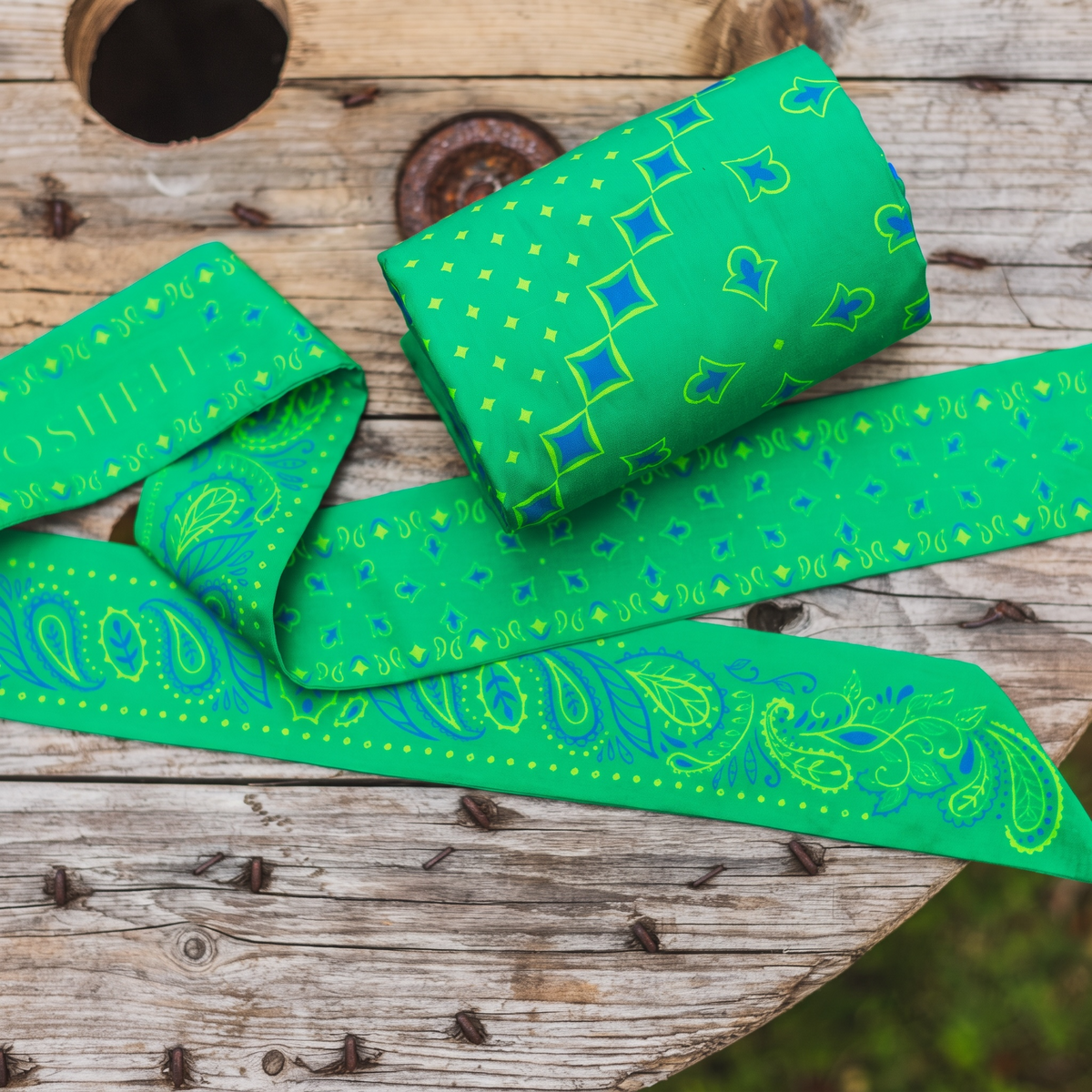 A bright green body bandana and scarf with blue and bright green paisley and diamond patterns, draped on a rustic wooden surface.