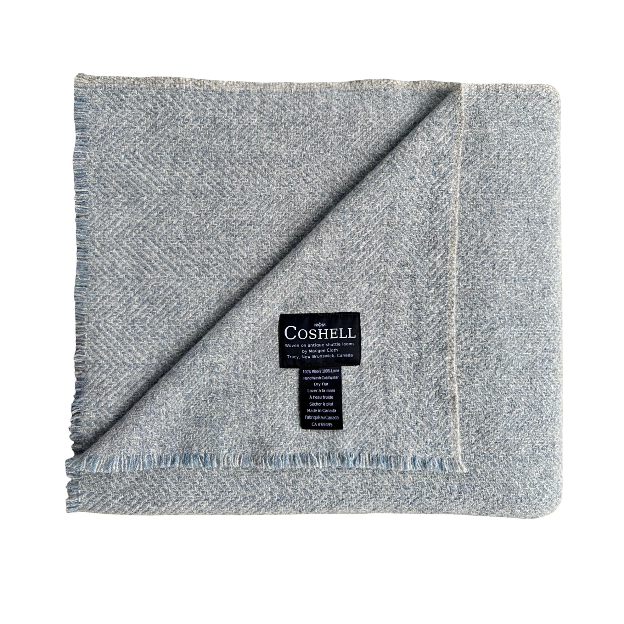 A folded light gray and blue herringbone woven blanket with fringed edges and a black Coshell brand label