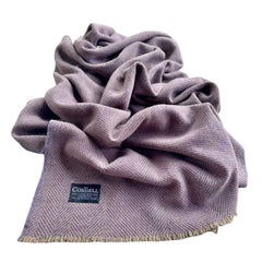 A dusty purple herringbone woven blanket with fringed edges and a black Coshell brand label