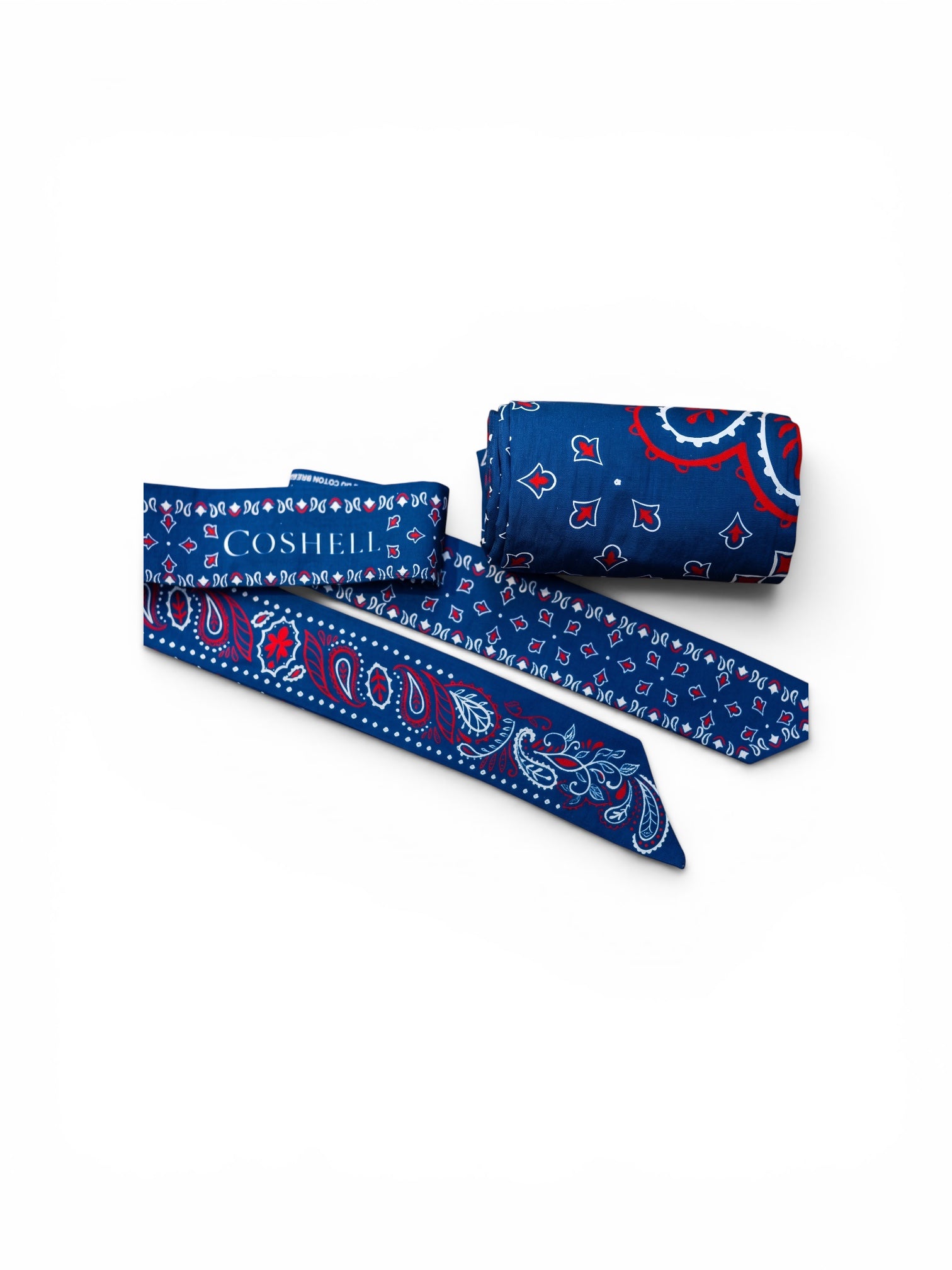 A blue patterned twilly scarf with red and white paisley motifs, shown partially unrolled next to a matching rolled body bandana sarong on a clean white background. The brand name 'COSHELL' is printed in white